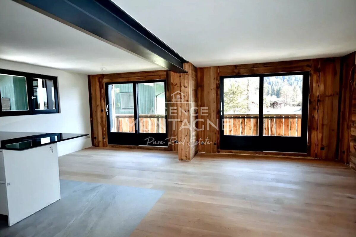 Modern chalet interior with wood-paneled walls, large windows framing mountain views, light wood floor, and a sleek counter.