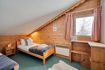 A cozy, wood-paneled attic bedroom with two single beds, plaid curtains, and a snowy window view, perfect for a ski chalet.