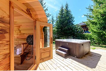 A hot tub sits on a wooden deck next to a sauna
