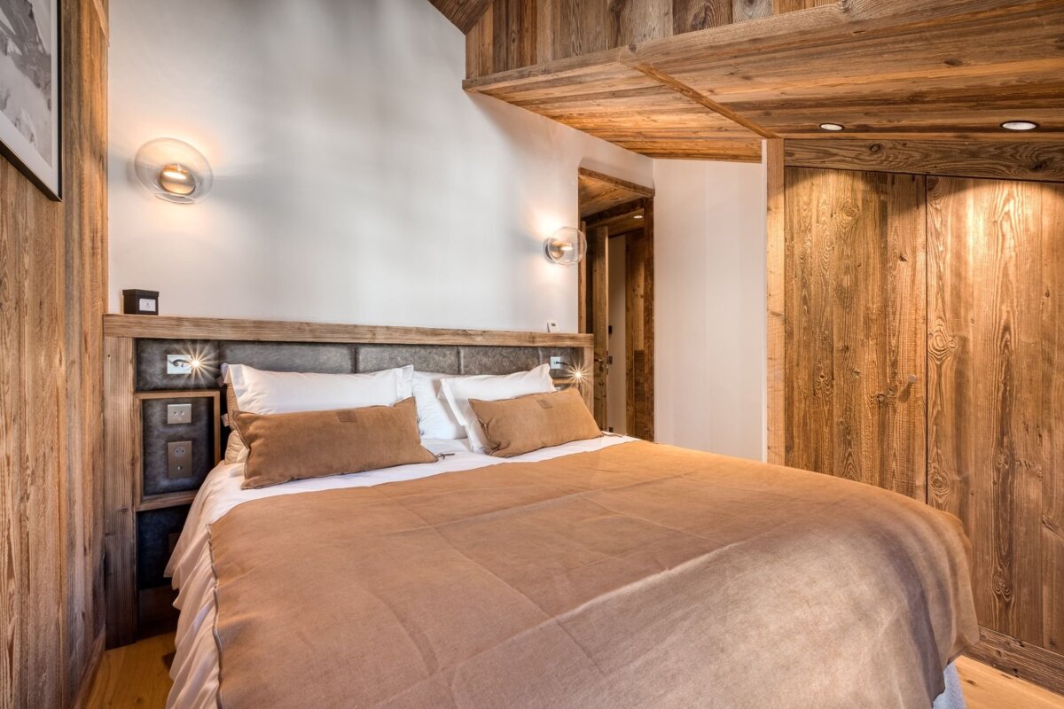 A modern alpine bedroom with rustic wood paneling, white walls, and a large bed with warm, neutral bedding, offering a cozy aesthetic.