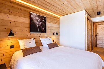 Cozy wood-paneled bedroom in a chalet, featuring a bed with white linens and a framed picture of a stag hanging on the wall.