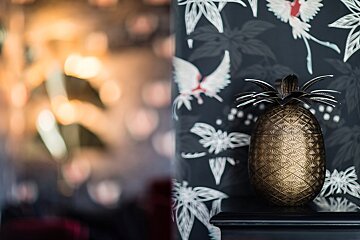 A pineapple shaped container sits on a shelf in front of a floral wallpaper