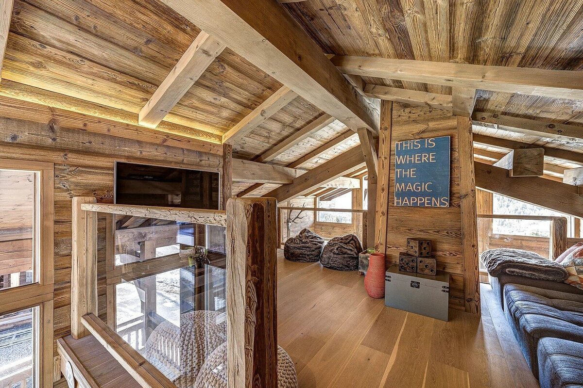 Cozy wooden loft in a rustic cabin with exposed beams, comfy seating, and a sign that reads 'this is where the magic happens'.