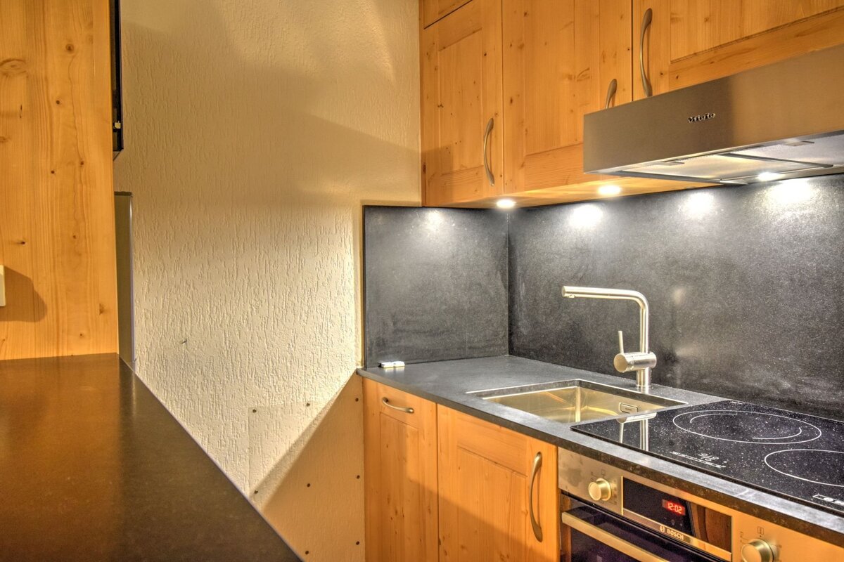 Cozy kitchen featuring light wooden cabinets, a dark countertop and backsplash, a stainless steel sink, and an induction cooktop.