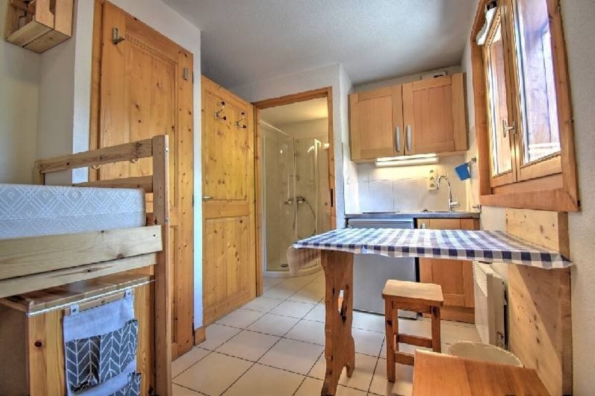 A small, rustic studio apartment with wooden furniture, a bunk bed, a dining table, and a small kitchen corner.