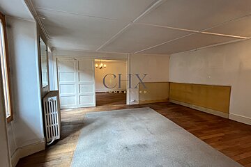 An empty room with hardwood floors, a large gray rug, a radiator, and double doors opening to another room in the background.