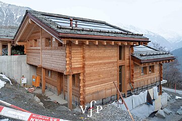 A wooden log chalet built on a mountain slope, featuring integrated solar panels on its roof.