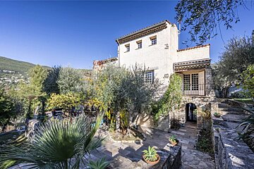 A rustic Mediterranean stone villa surrounded by olive trees and stone terraces under a clear blue sky.