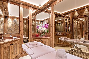 A luxurious spa room in a rustic wood chalet style, featuring multiple massage beds, mirrored walls, stone accents, and orchid decor.