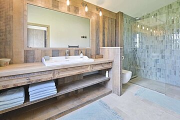 A modern rustic bathroom featuring a long wooden vanity with a white sink, large mirror, and a spacious shower with light blue subway tiles and glass enclosure.