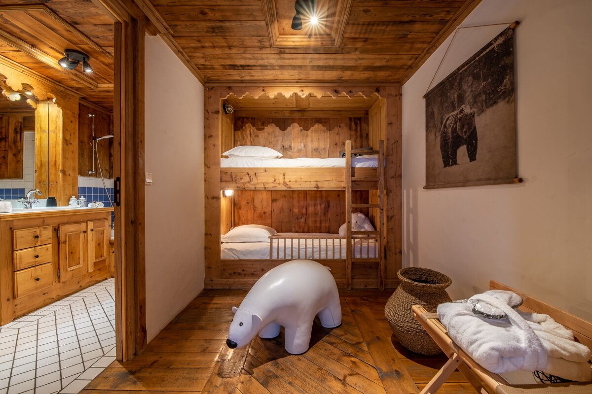 Rustic wooden room with built-in bunk beds, a polar bear toy, and a bear tapestry. An adjoining bathroom is visible on the left.