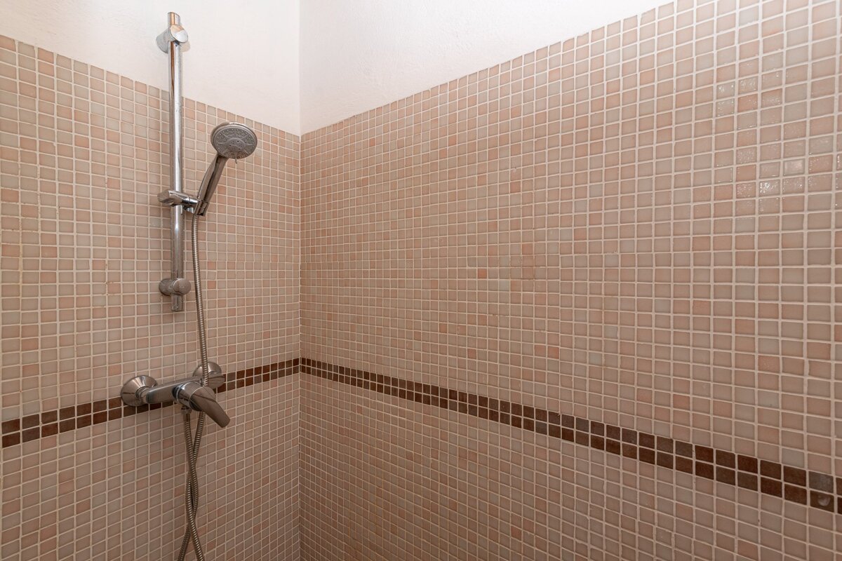 A shower stall with light brown mosaic tiles, featuring a dark brown accent stripe, silver shower head, and mixer tap.
