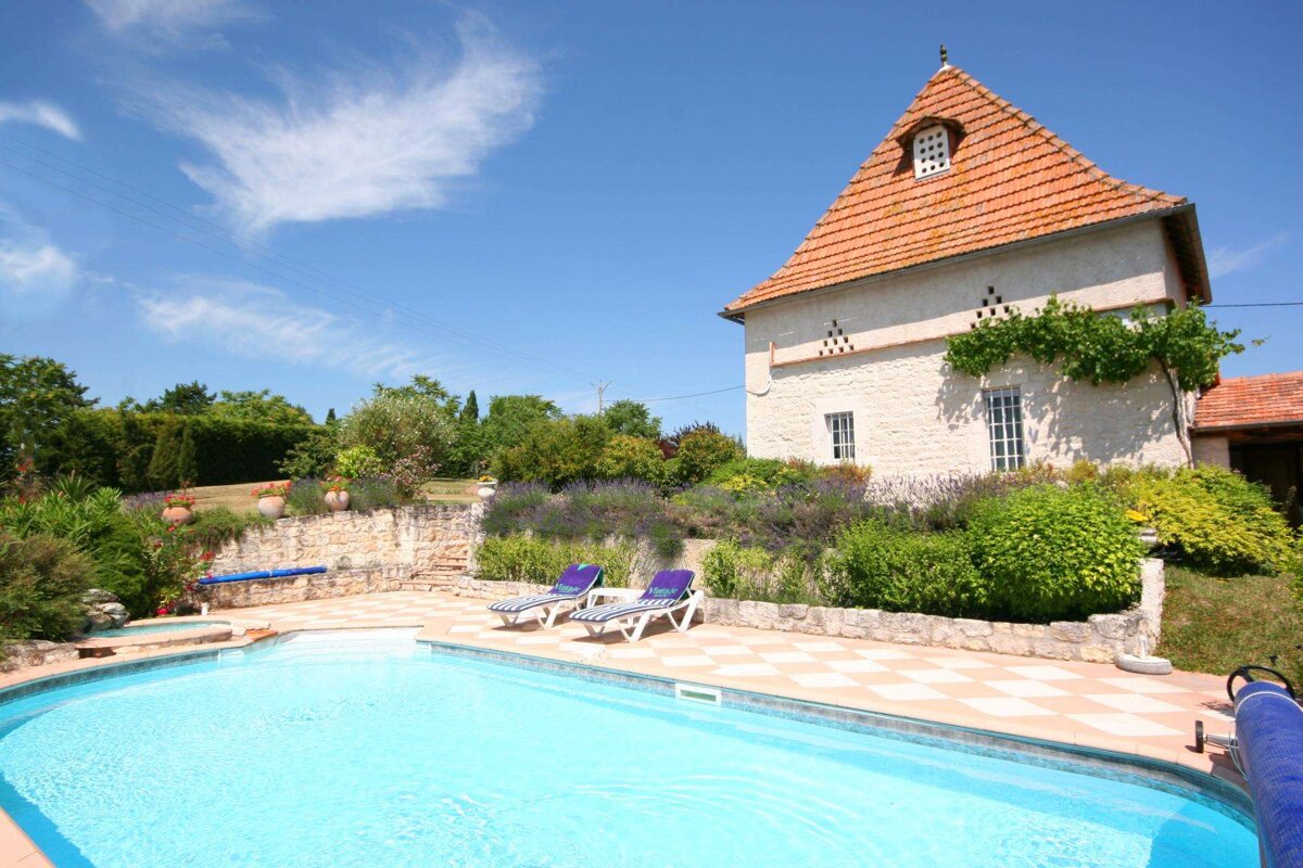A swimming pool in front of a house with a red tiled roof