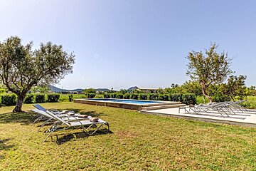 A row of lounge chairs sit in a grassy area near a swimming pool