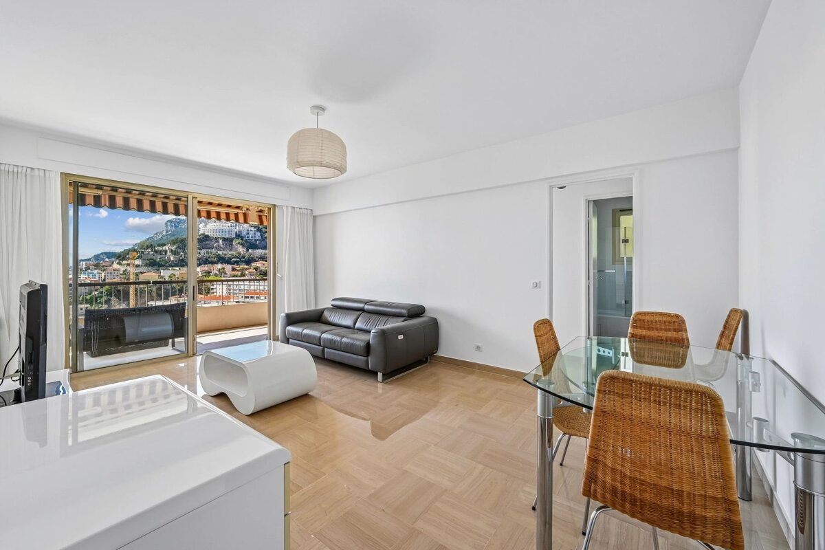 Spacious living/dining room with a black sofa, glass table, and balcony showcasing a stunning city and mountain vista.