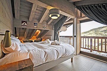 Cozy chalet bedroom with wooden beams, a plush bed, and a balcony offering stunning mountain views.