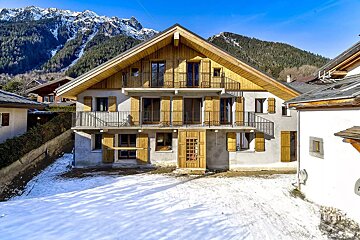 A house with snow on the ground and mountains in the background