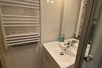A clean bathroom featuring a white sink, chrome faucet, blue soap dispensers, a mirror, and a white heated towel rack on tiled walls.