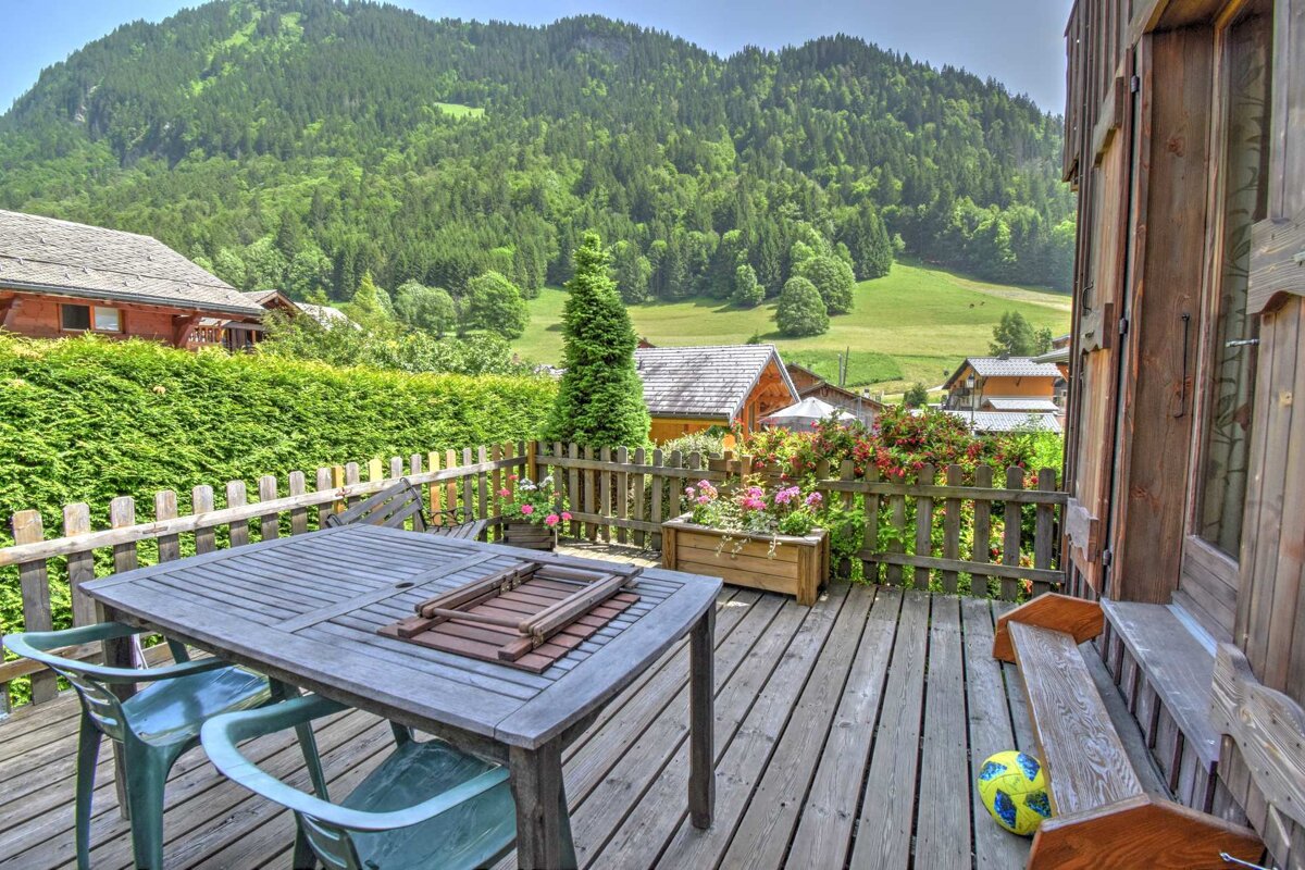 A table and chairs on a deck with a mountain in the background