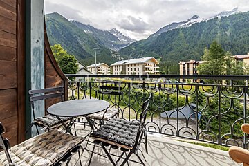 A balcony with a table and chairs and mountains in the background