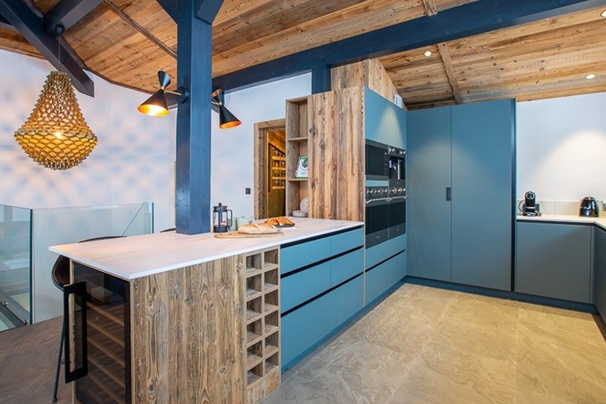 Modern rustic kitchen featuring teal cabinets, wood ceilings, a white-topped island, and a distinctive woven pendant light.