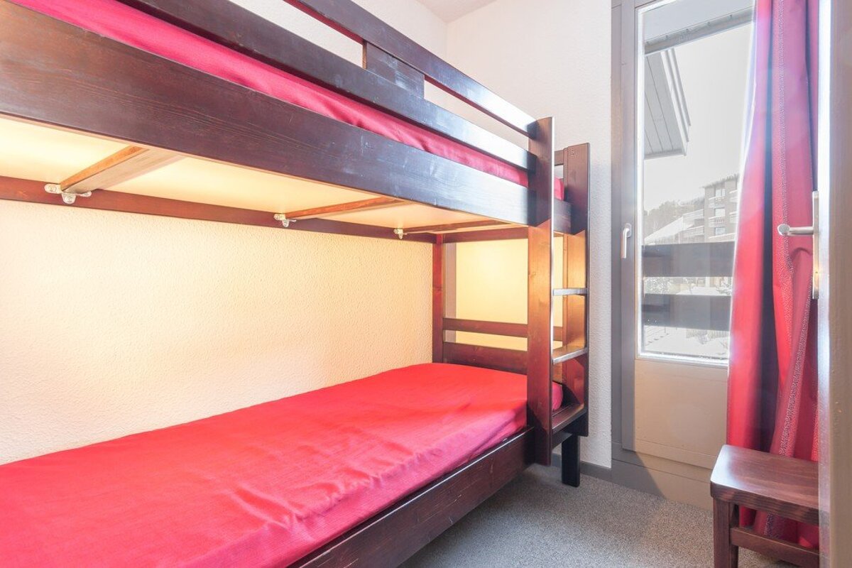 A bunk bed with red sheets and a window