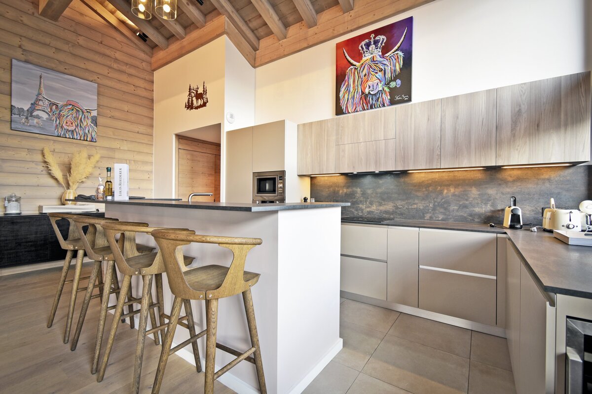 Modern chalet kitchen featuring a breakfast island with four wooden bar stools and vibrant artwork of highland cows on the walls.