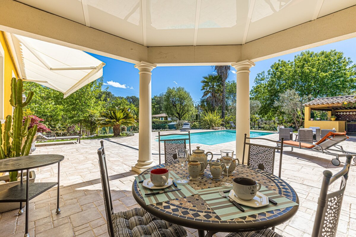A patio with a table and chairs and a swimming pool in the background