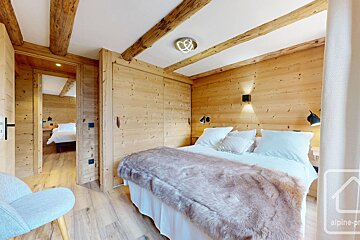 Cozy, wood-paneled bedroom with exposed beams, a large bed with a furry throw, modern ceiling light, and another similar room visible.