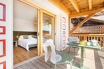 A balcony with a table and chairs and a bed in the background