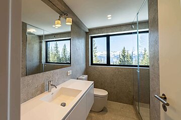 Modern bathroom with a sleek vanity, large mirror, and stunning window views of snow-capped mountains and a forest.