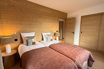 A cozy rustic bedroom featuring twin beds with reddish blankets, set against a light wood paneled wall and matching doors.