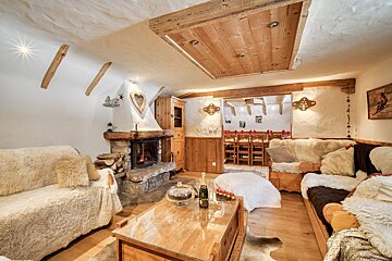Inviting chalet living room featuring a warm stone fireplace, plush fur throws, wooden ceiling, and a peek into a dining area.