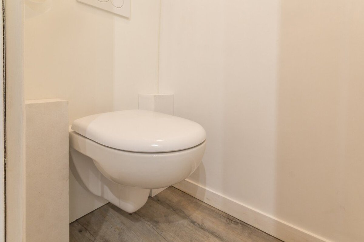 A white toilet is mounted to a white wall