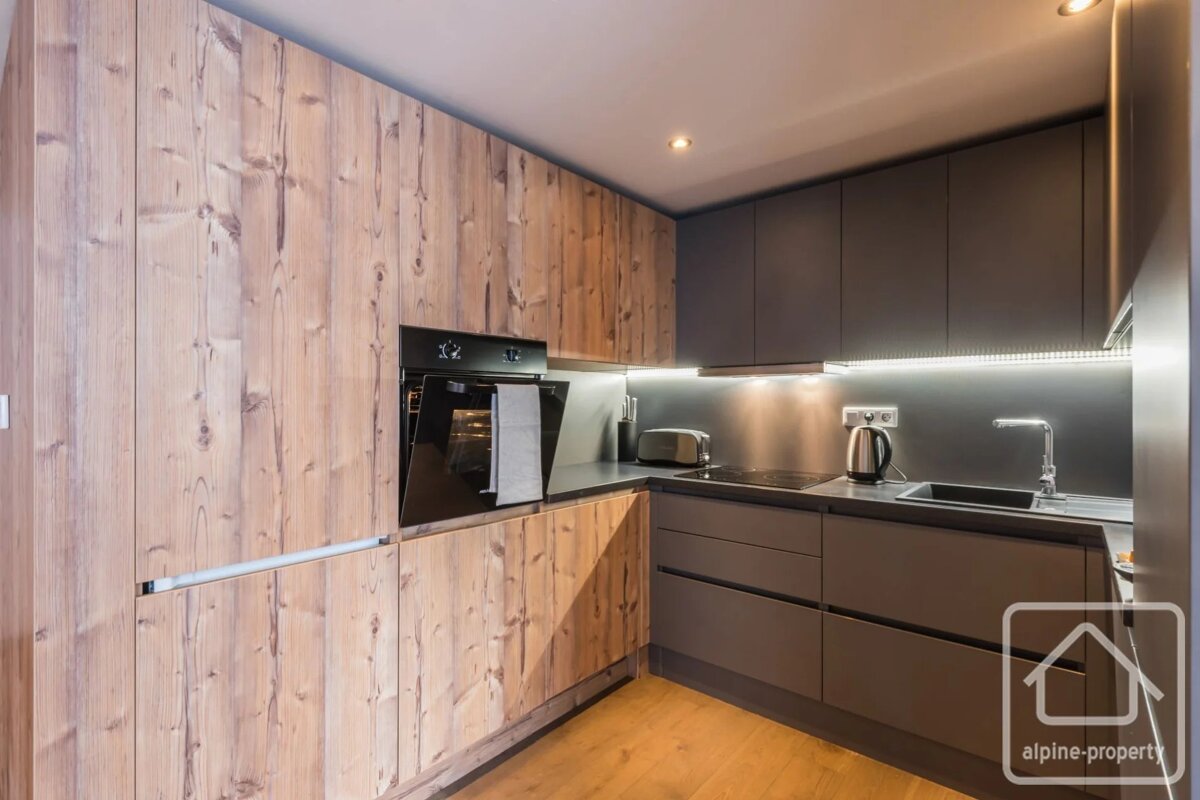 A modern kitchen with light wood cabinetry on the left and sleek dark grey cabinets, countertop, and appliances on the right.