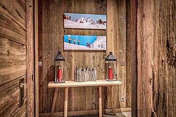 Rustic wooden hallway with a console table, two lanterns with red candles, and two framed skiing pictures on the wall.