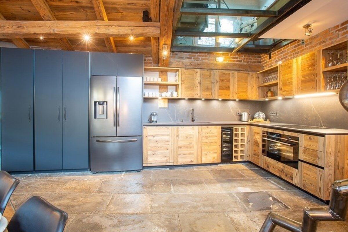 Rustic kitchen with wooden cabinets, stone floors, exposed beams, a stainless steel fridge, and a glass ceiling.