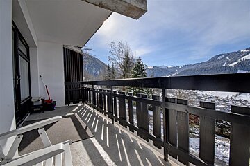 A sunny balcony overlooks a snow-covered mountain valley and village under clear blue skies, ideal for a winter retreat.