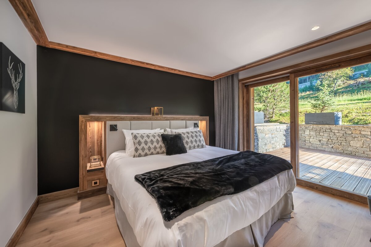 Modern chalet bedroom featuring a black accent wall, wooden headboard, and glass sliding doors opening to an outdoor wooden deck.