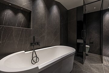 Modern dark-themed bathroom with a white freestanding tub, black fixtures, and dramatic dark marble tiles.