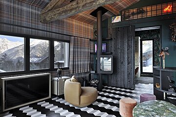 A chic mountain chalet interior with plaid ceiling, 3D chevron floor, modern fireplace, and stunning snowy mountain views from large windows.