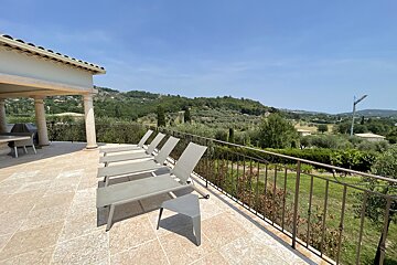 A row of lounge chairs on a balcony overlooking a lush green hillside