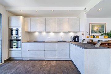 Sleek, modern kitchen with light gray textured cabinets, dark wood floor, built-in appliances, and a long counter with decorative elements.