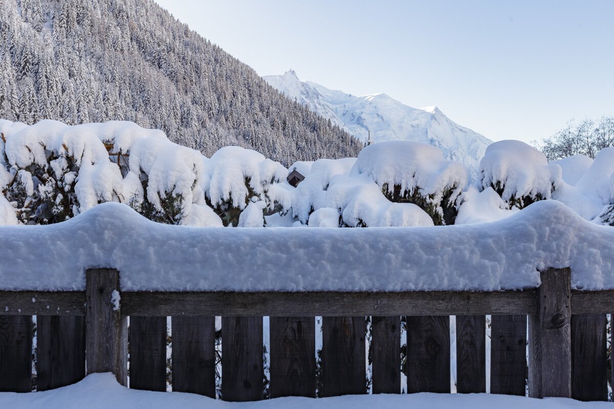 A wooden fence covered in snow with mountains in the background