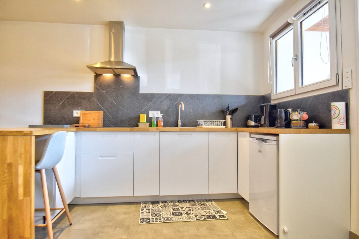 Modern kitchen featuring white cabinets, wooden countertops, a dark grey backsplash, and a patterned rug on the floor.