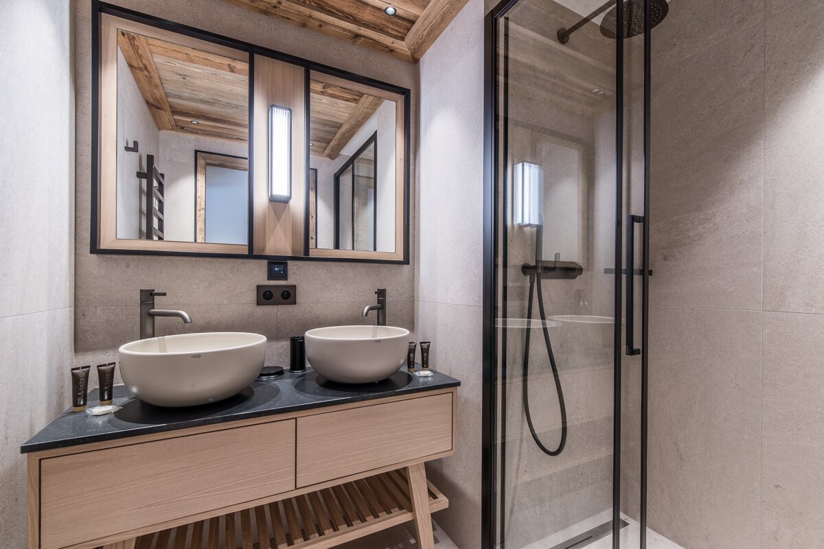 Modern rustic bathroom with a double-sink wooden vanity, dual mirrors, and a sleek black-framed glass shower.