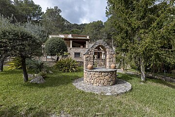 A stone well sits in the grass in front of a house
