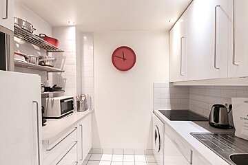 A kitchen with white cabinets and a red clock on the wall