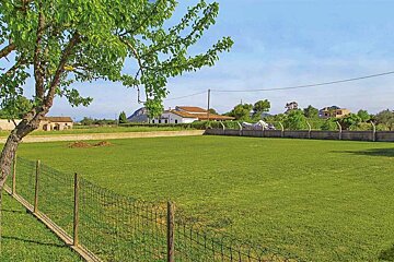 A fence surrounds a lush green field with a house in the background