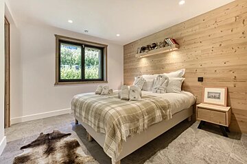 Cozy modern bedroom featuring a wood-paneled accent wall, a plaid blanket, and a cowhide rug on the grey tile floor.